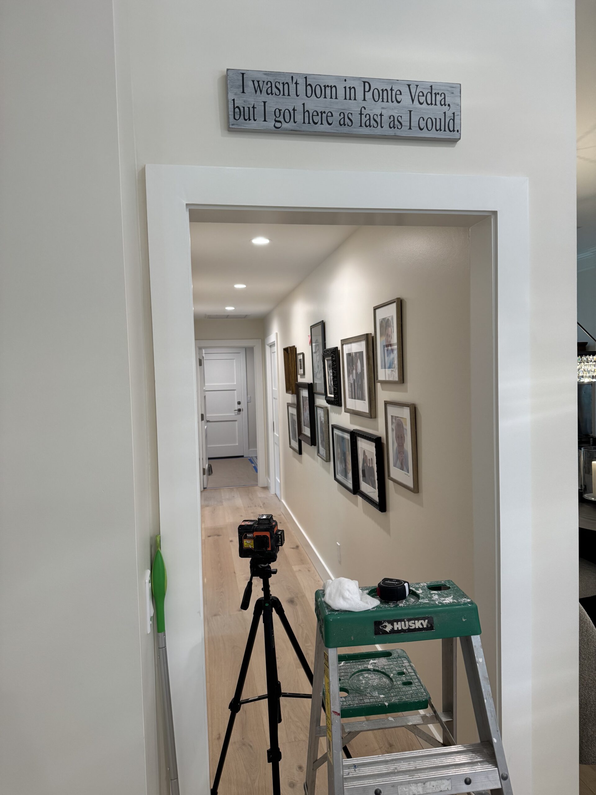 Ladder, laser level, and tools set up in a Ponte Vedra hallway for gallery wall photo installation